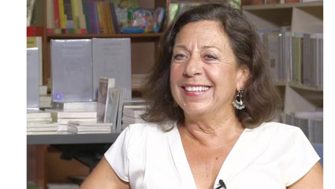 Marsha Familaro Enright laughing during an interview, bookshelves behind her.